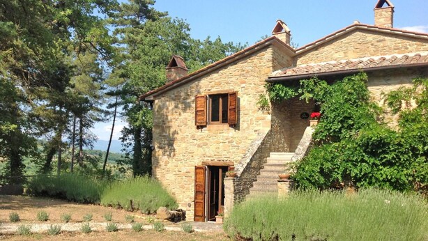 A stone house with a wooden door and shutters, surrounded by greenery and trees. - Casale Mollina 6 2 (Anghiari)