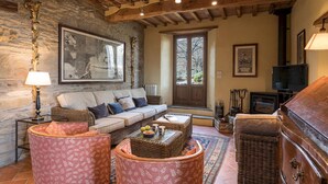 A cozy living room with a stone wall, a sofa, wicker furniture, a fireplace, and a television. - Casale Mollina 6 2 (Anghiari)