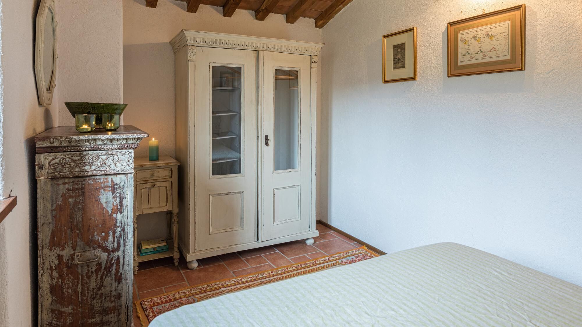 A bedroom with a bed, a wardrobe, a small cabinet, and a decorative mirror.