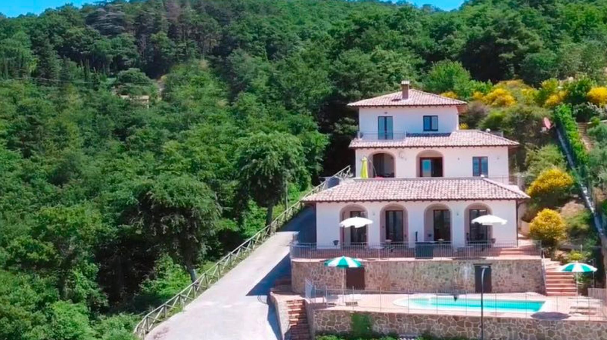 Uma vila de dois andares com fachada de pedra, piscina e escadaria que leva à entrada.