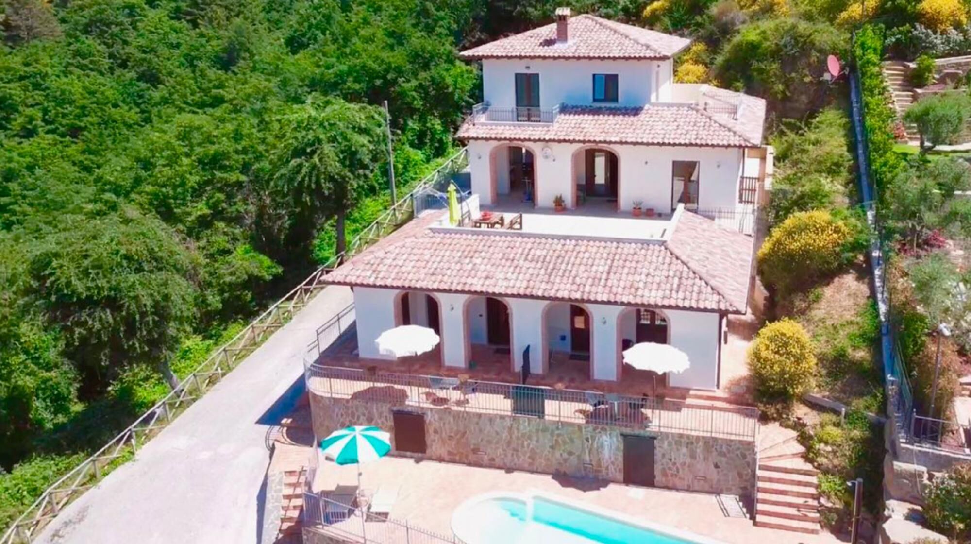 Uma vila de dois andares com piscina, rodeada por vegetação exuberante.