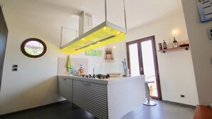 A modern kitchen with a central island, a hanging light fixture, and a view of the outdoors. - Villa Maggiorana 10 (Lisciano Niccone)