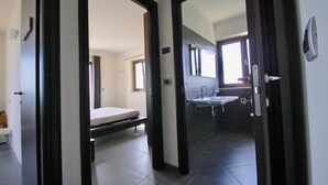 A hotel room with a bed, a bathroom with a sink and mirror, and a view of the hallway. - Villa Maggiorana 10 (Lisciano Niccone)