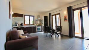 A modern living room with a sofa, dining table, and chairs. There is a kitchen area with cabinets and appliances. - Villa Maggiorana 10 (Lisciano Niccone)