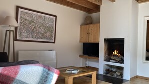 Una sala de estar acogedora con chimenea, techo de madera, un mapa enmarcado en la pared y una mesita con un libro.