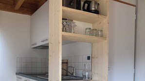 Cocina con armarios de madera, una encimera y un lavamanos. Hay una silla y una mesa en primer plano.