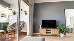 Ein modernes Wohnzimmer mit einem Flachbildfernseher auf einem Holzboden, einem Korbstuhl und einem Blumentopf.