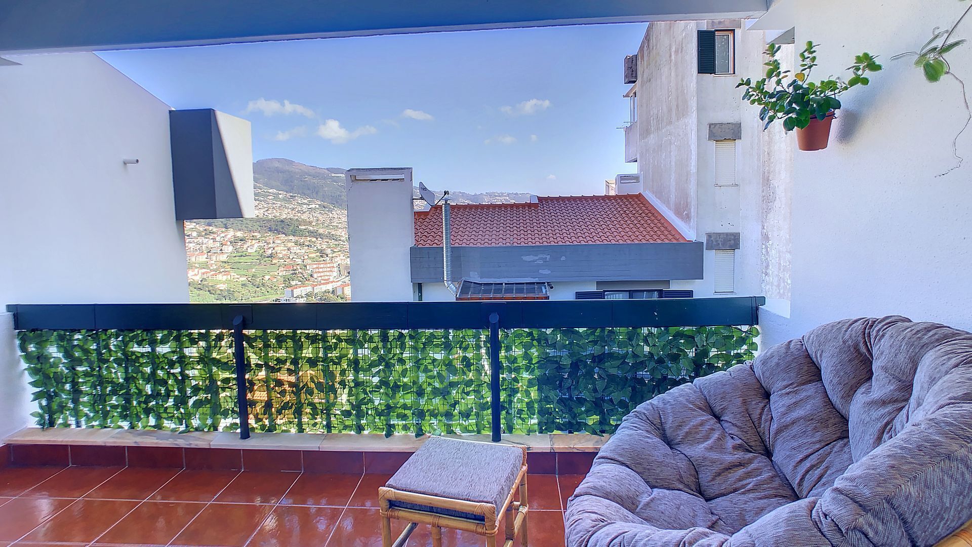 A balcony with a view of a cityscape, a cushioned chair, and a small table.