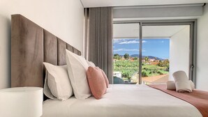 Une chambre d’hôtel moderne avec un grand lit, une lampe de chevet et une vue sur le paysage urbain, visible à travers une porte-fenêtre coulissante.