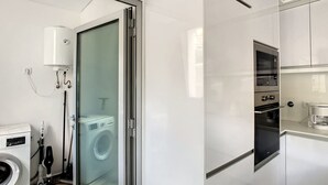 Une cuisine moderne dotée d’appareils électroménagers intégrés, une porte vitrée donnant sur un espace buanderie et un chauffe-eau visible.
