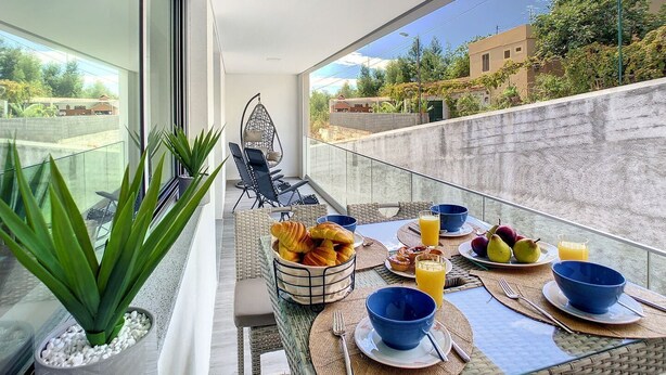 Un balcon avec une table à manger dressée pour le petit-déjeuner, comprenant des fruits, des viennoiseries et une boisson.