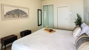 Une chambre à coucher avec un grand lit, une table de chevet, un miroir, une porte et une œuvre d’art accrochée au mur.