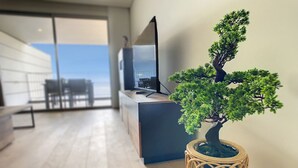 Un salon moderne avec un plancher en bois, une grande fenêtre et un bonsaï dans un pot en osier.