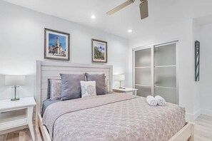 A bedroom with a bed, nightstands, a ceiling fan, and a sliding glass door closet. - A Shore Thing: Holidays by the Beach! (St. Augustine Beach)