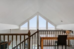 A dining area with a wooden table and chairs, a black chair, and a wooden railing. - A Shore Thing: Holidays by the Beach! (St. Augustine Beach)
