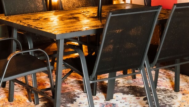 Un espace de restauration en plein air avec une table en bois et des chaises noires, entouré de guirlandes lumineuses et d’une pergola blanche.