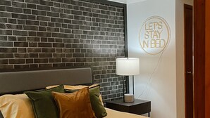 Un lit bien fait, agrémenté d’un plaid jaune, d’une tête de lit moderne et d’une pancarte fixée au mur sur laquelle on peut lire : « RESTONS AU LIT ».