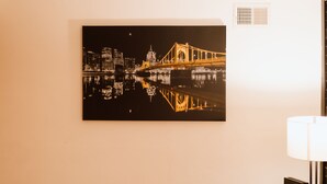 Une vue encadrée d’un paysage urbain avec un pont se reflétant dans l’eau, un lampadaire et une grille d’aération sur le mur.