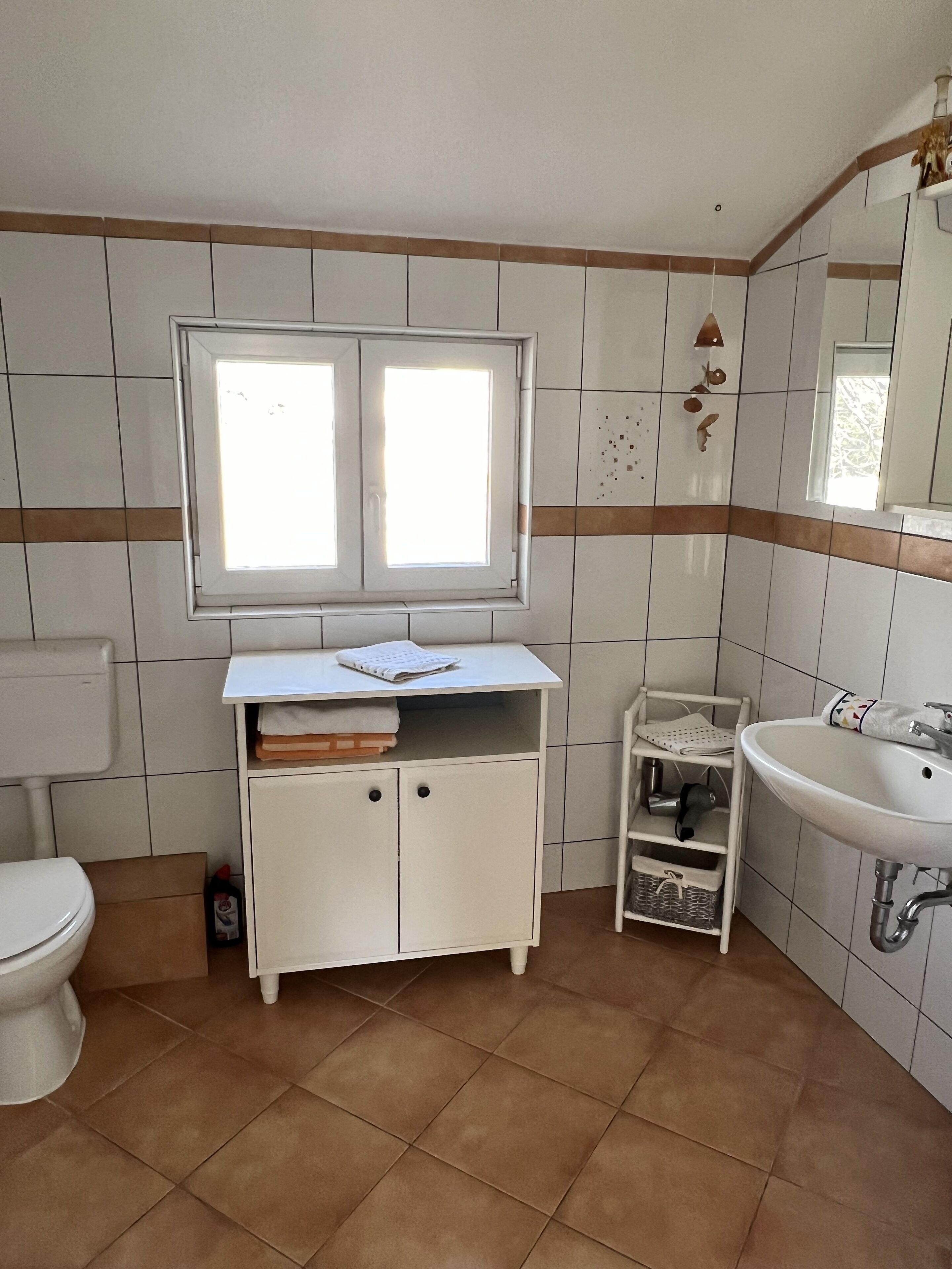 Une salle de bain avec des toilettes, un lavabo, une fenêtre et un meuble.