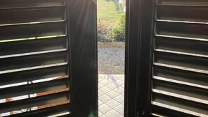 A view through a door with horizontal slats, leading to an outdoor area with a tiled floor and a lamp post.