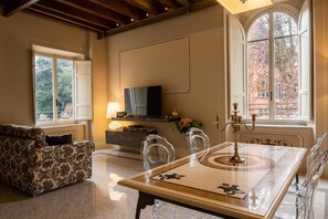 A living room with a sofa, a dining table with chairs, a TV, and a window with a view of trees. - Charming flat in the heart of Lucca (Lucca)
