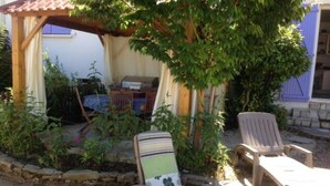 Jardí amb dos seients de relaxació, una pérgola i una taula sota un arbre.