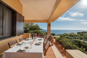 An outdoor dining area with a table set for six, overlooking a scenic view of the sea and greenery.