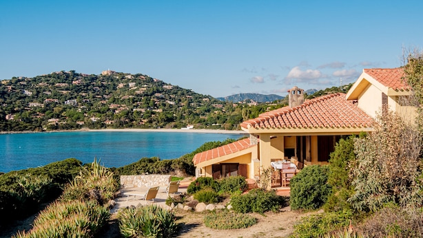 Una casa costera con un patio, vista al mar y una colina con edificios.