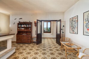 Una habitación con piso estampado, una estantería, un rincón de comedor con sillas de mimbre y vistas a través de una puerta abierta.