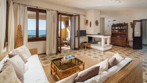Amplia sala de estar con sofá, mesa de centro y estantería. Se ve el océano a través de amplias ventanas.