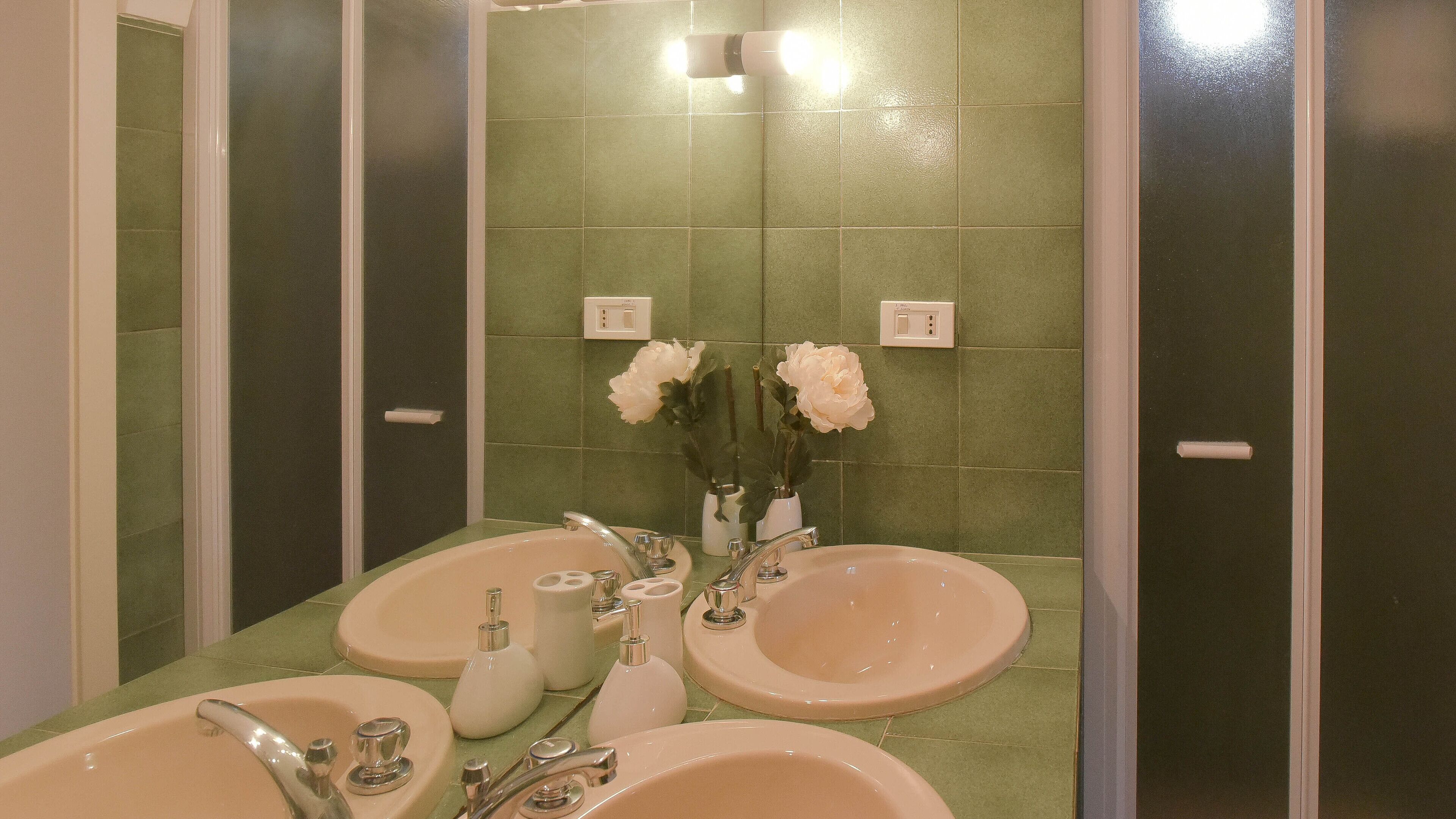 A bathroom with two sinks, a mirror, and green tiled walls.