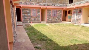 A courtyard with a paved walkway, a grassy area, and a building with multiple doors and windows.