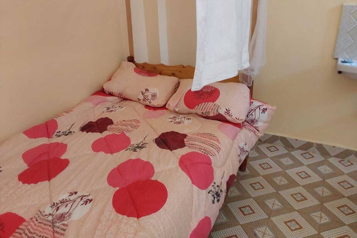 Uma cama com colcha florida e duas almofadas, um dossel branco e um piso estampado.