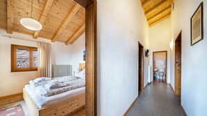 A bedroom with a wooden bed, a window with curtains, a radiator, and a hallway leading to a bathroom. - Apartment "Eggerhof Familienparadies" with Mountain View, Lake Access & Wi-Fi (Verano)