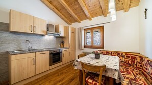 A kitchen with wooden cabinets, a built-in oven, and a dining area with a patterned tablecloth. - Apartment "Eggerhof Familienparadies" with Mountain View, Lake Access & Wi-Fi (Verano)