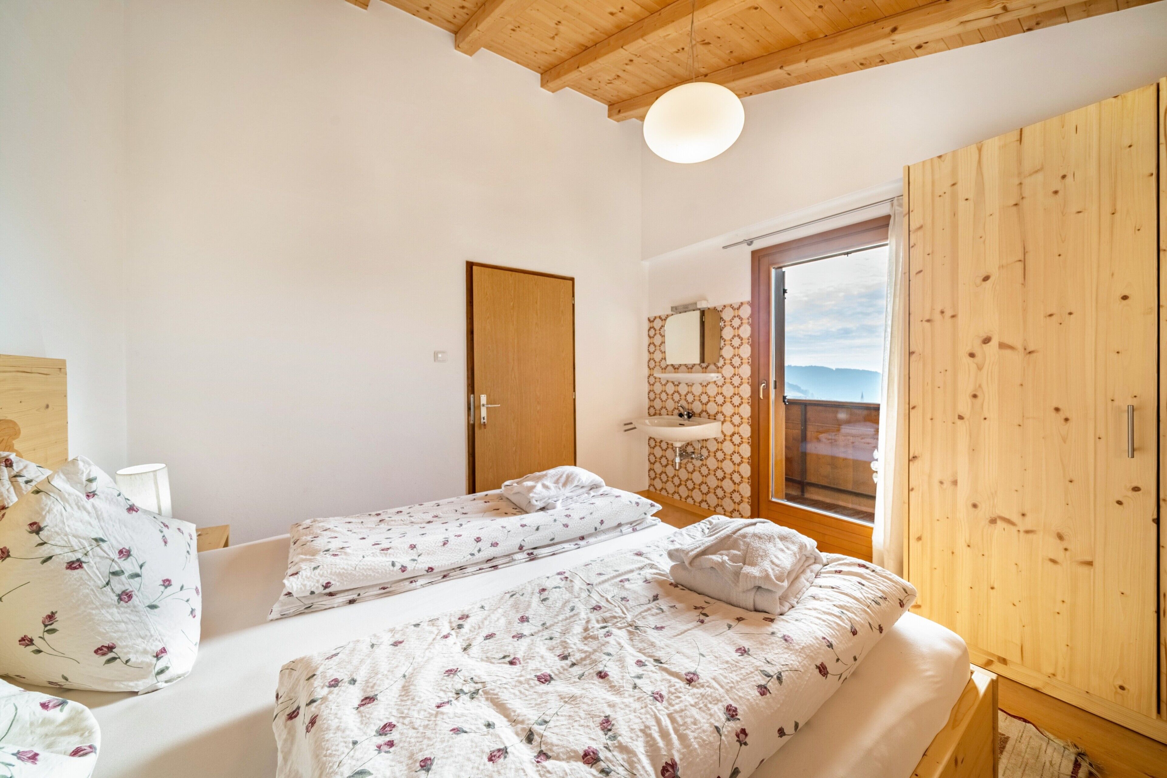 Un dormitorio con dos camas, un armario de madera, un baño con lavabo y espejo, y vistas al exterior.