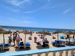 A beach with sun loungers, umbrellas, and people.