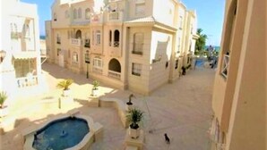 Um pátio com piscina, um edifício com varandas e céu claro.