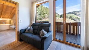 Habitació moderna amb un sofà gris, un sostre de fusta i un balcó que mostra un paisatge boscós.