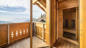 A wooden balcony with a view of mountains, a sauna, and a wooden deck.