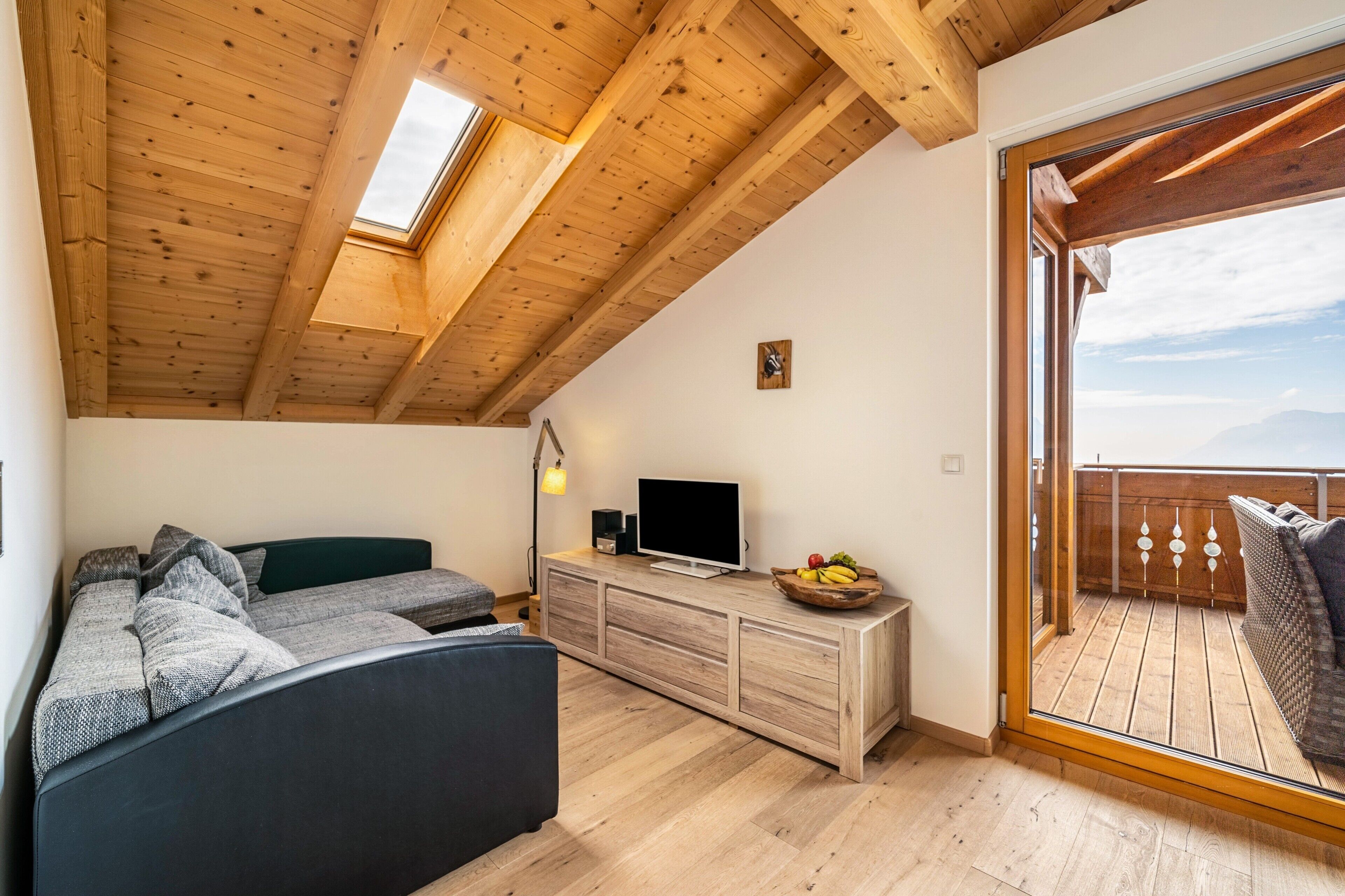 A loft-style room with a wooden ceiling, a sofa, a TV, and a balcony with a view.