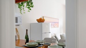 Un comedor con una mesa dispuesta para cuatro personas, un microondas, un refrigerador y un cuadro en la pared.
