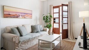 Una sala de estar con sofá, mesa de centro, planta, cuadro y puerta.