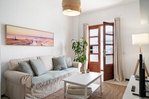 Una sala de estar con sofá, mesa de centro, planta, cuadro y puerta.