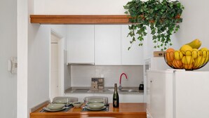 Una pequeña cocina con armarios blancos, encimera de madera, un lavabo, un refrigerador y un bol de fruta sobre la encimera.