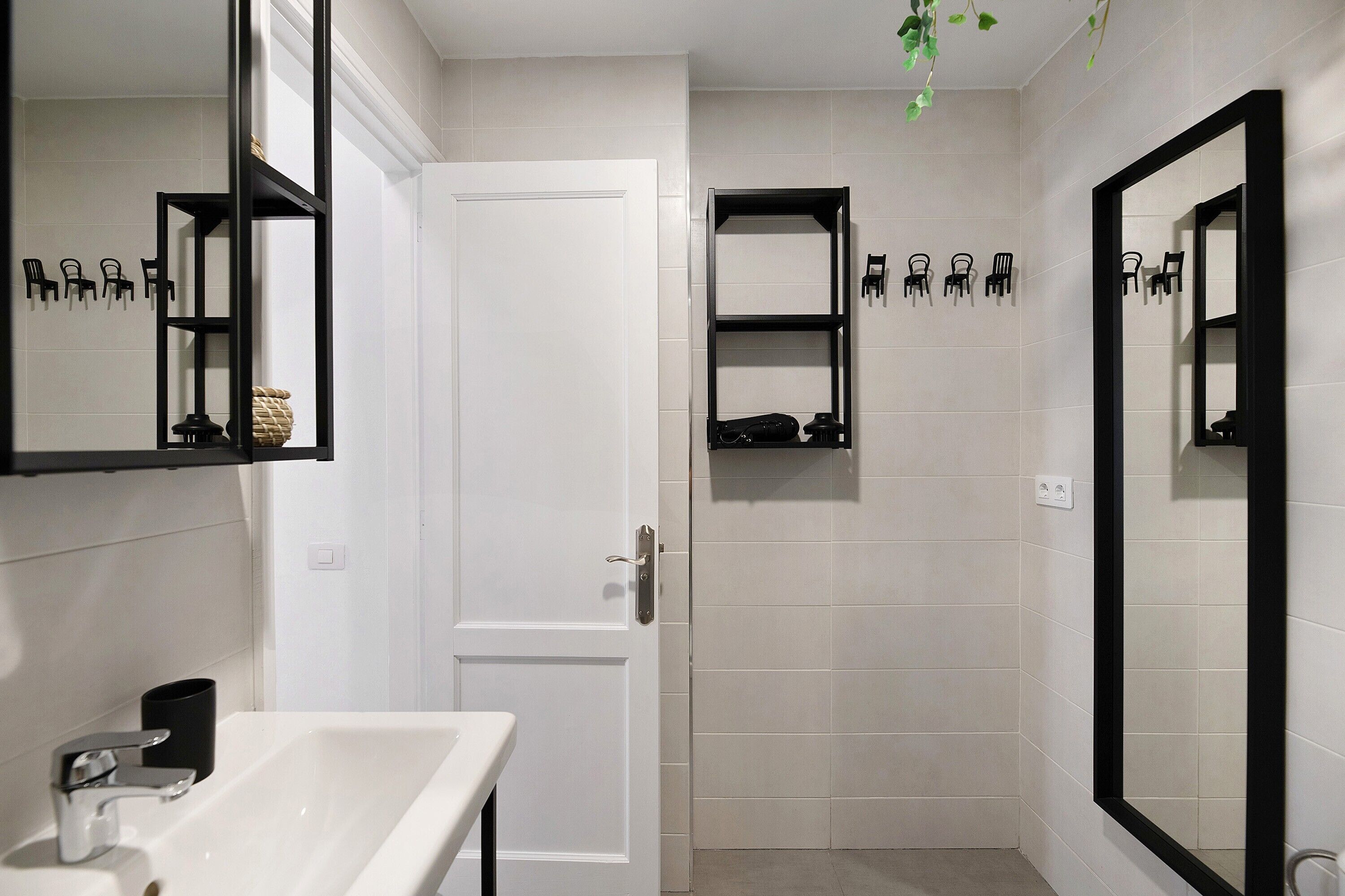 Een badkamer met een wit wastafel, een deur en twee spiegels met zwarte omlijsting.