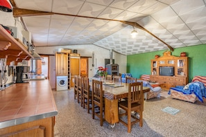 A kitchen with a dining table, chairs, a washing machine, and a TV in a living area with a green wall and wooden furniture.