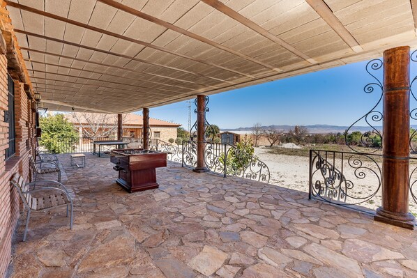 A covered patio with stone flooring, outdoor furniture, and a pool table.