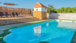 En swimmingpool med en stenhus, liggestole og et træhegn.
