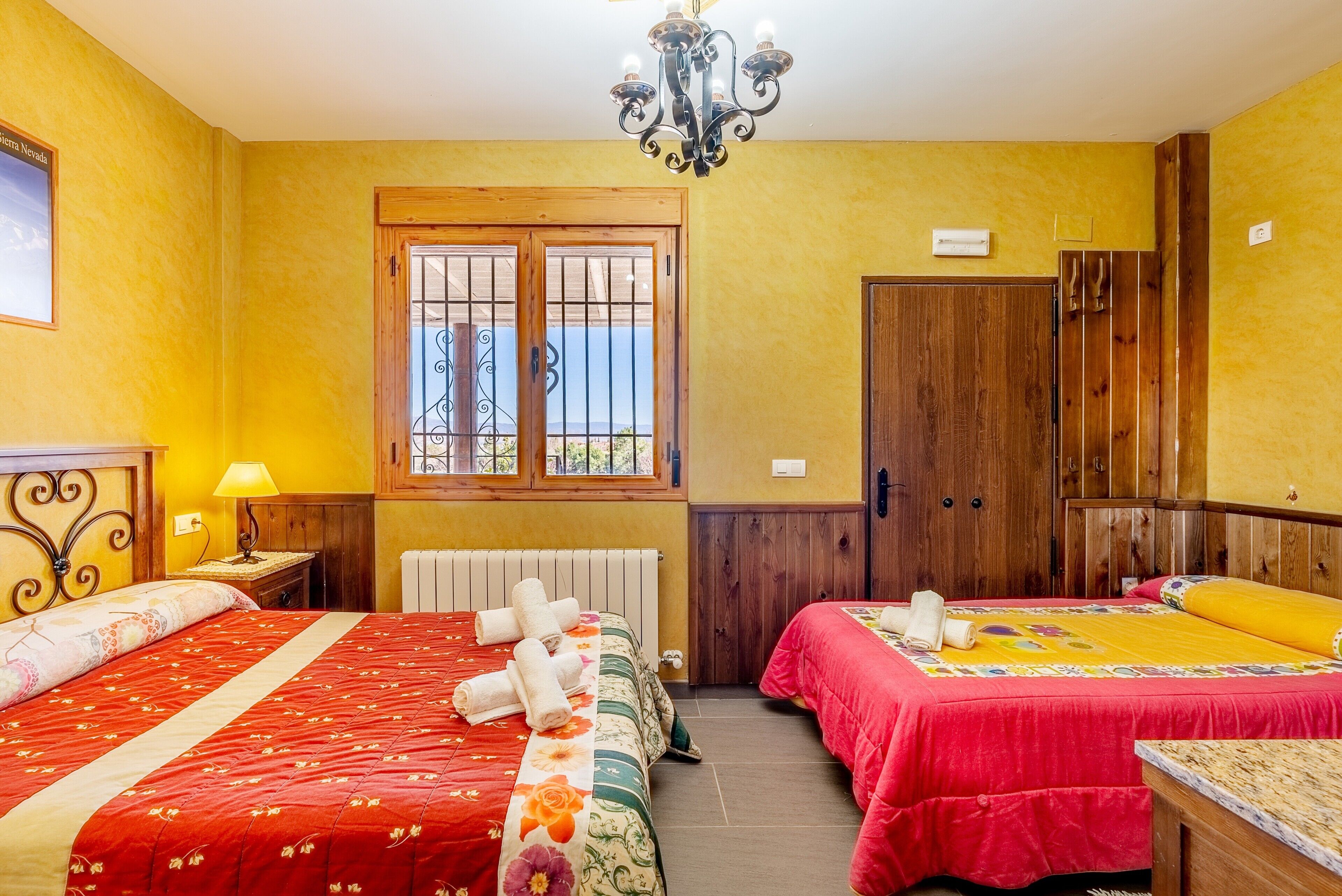 A hotel room with two beds, a wooden wardrobe, a chandelier, and a window with bars.